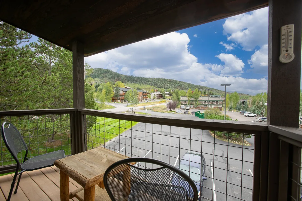 This image depicts a wooden table and black chairs on an outdoor patio, with a sweeping mountain view and a cloudy sky in the background. The setting is casual and inviting, perfect for relaxation, remote work, or enjoying a break with inspiring scenery.