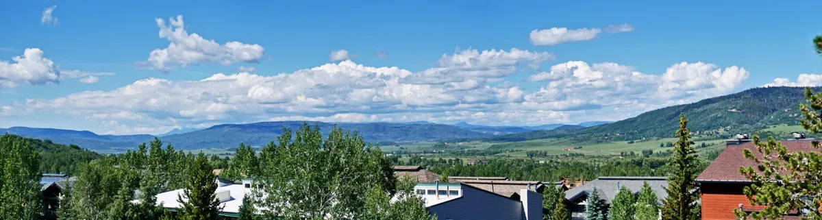 A sweeping view of an expansive mountain range and lush green valley beneath scattered clouds. The landscape captures the region’s natural beauty, with the panoramic horizon evoking the allure of sunset watching and peaceful moments.