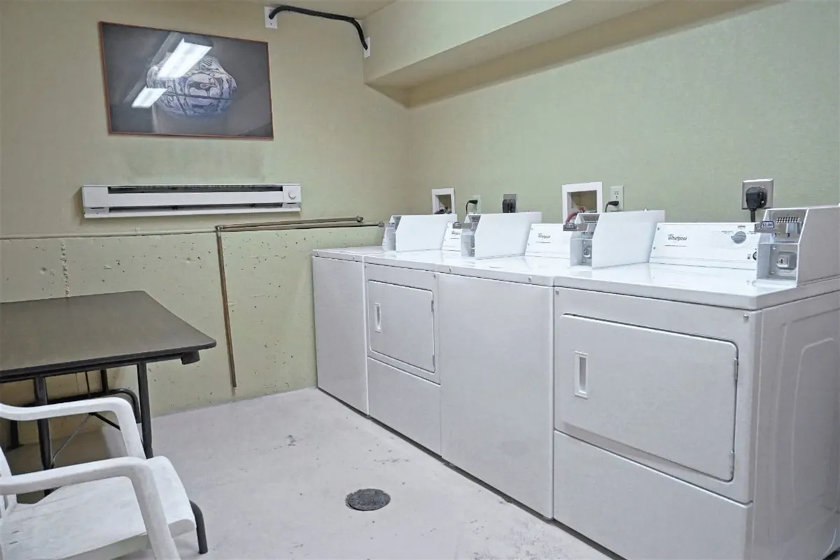 A practical, well-lit shared laundry room with washing machines, dryers, and a small seating area, providing convenience for extended stays or quick refreshes.