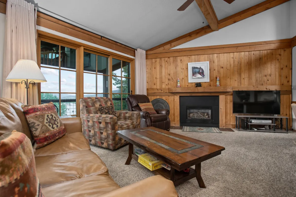 This interior image features a spacious living area with a prominent fireplace, large windows that flood the room with natural light, a comfortable seating area including plush recliners, and distinct wooden accents. The setting is warm, inviting, and ideal for socializing or relaxing.