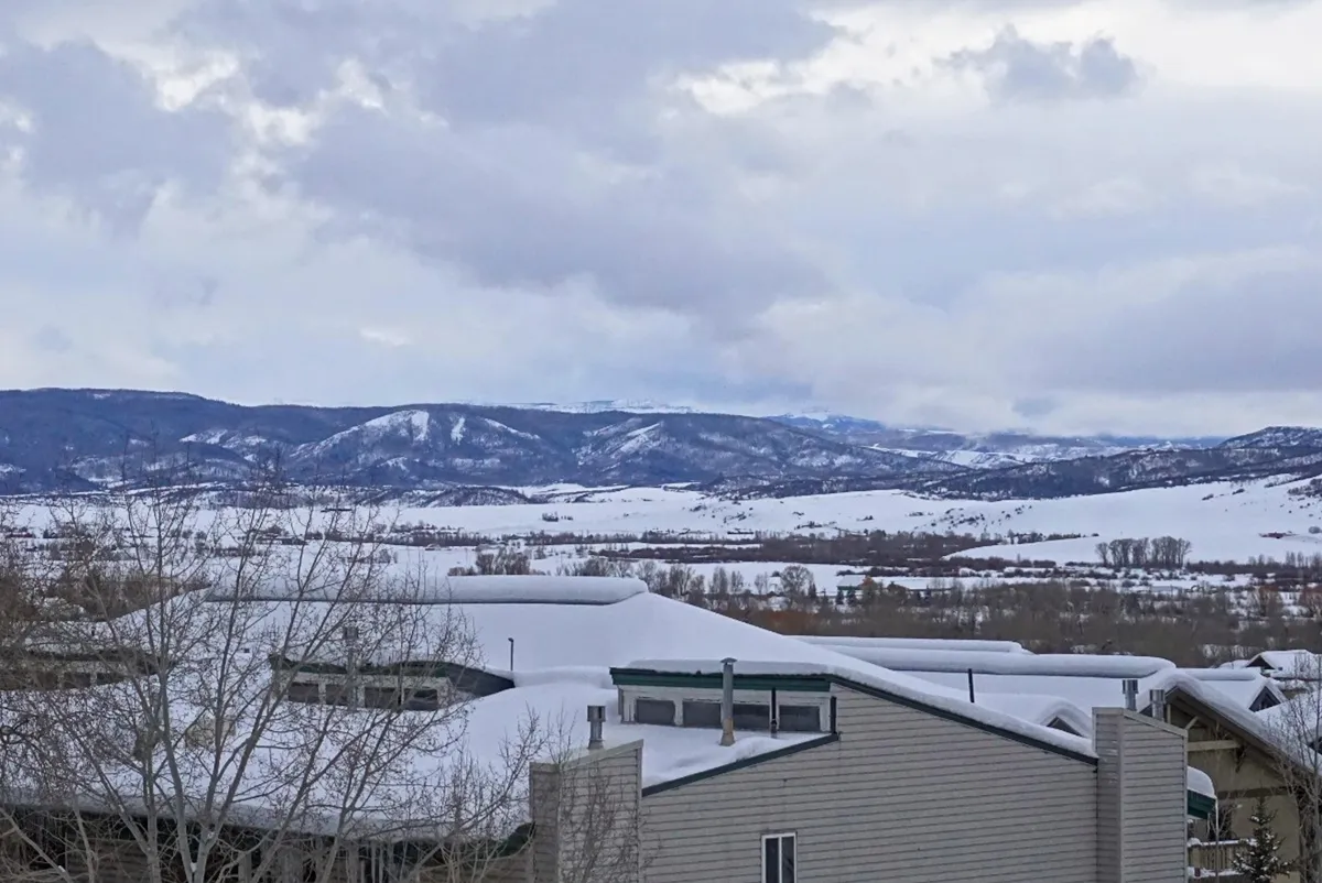 An elevated, panoramic view of snow-blanketed mountains and rooftops captures the beauty of Steamboat in winter. Bare trees and tranquil scenery evoke a sense of adventure and relaxation after outdoor activities.