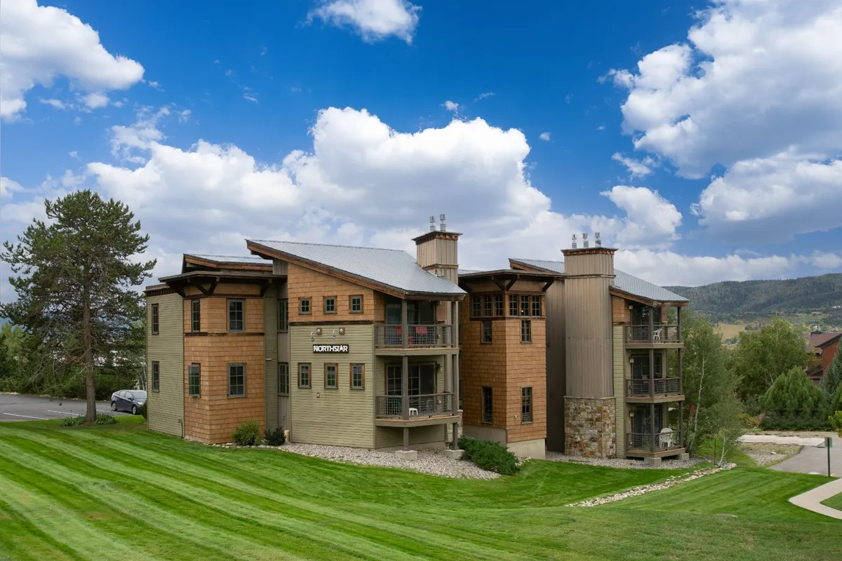 This image displays the condo's modern architecture set amidst a beautifully landscaped lawn, with large windows and stone accents. The porch offers a welcoming space for outdoor relaxation, while the surrounding greenery hints at the area's natural beauty and nearby trails.