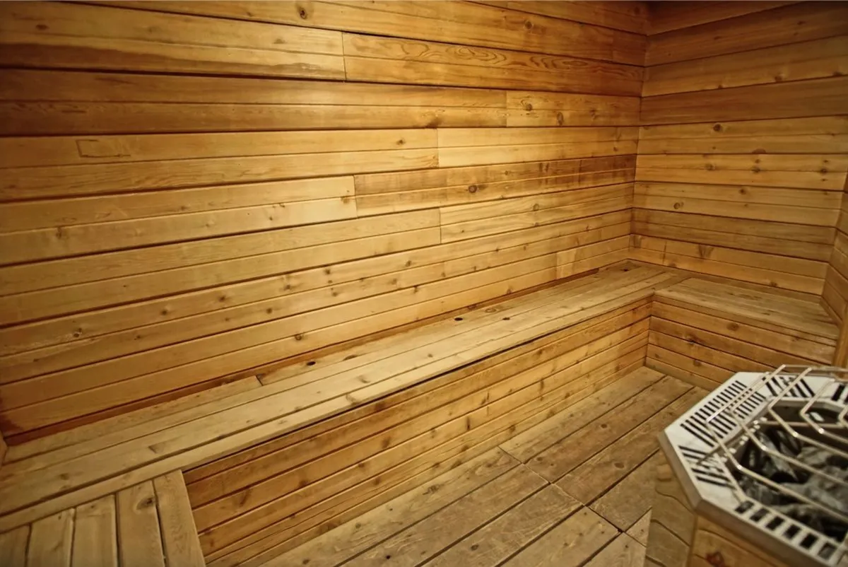 A serene sauna room with wooden benches and walls, complemented by a central heating element. The space is cozy yet spacious, ideal for post-adventure relaxation or a peaceful moment of solitude.